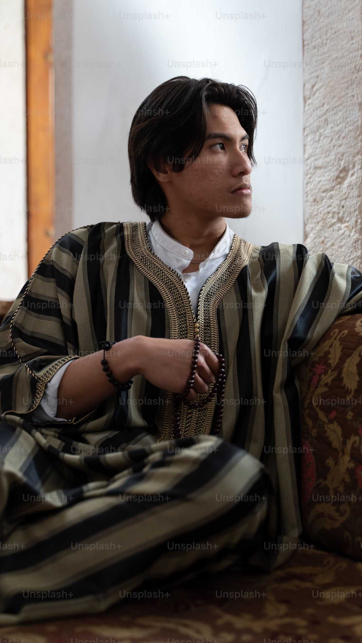 man in striped robe holding 
                                    polished brown beads