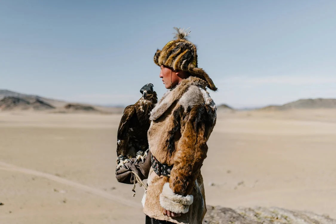 man dressed in furs with hunting falcon in desert